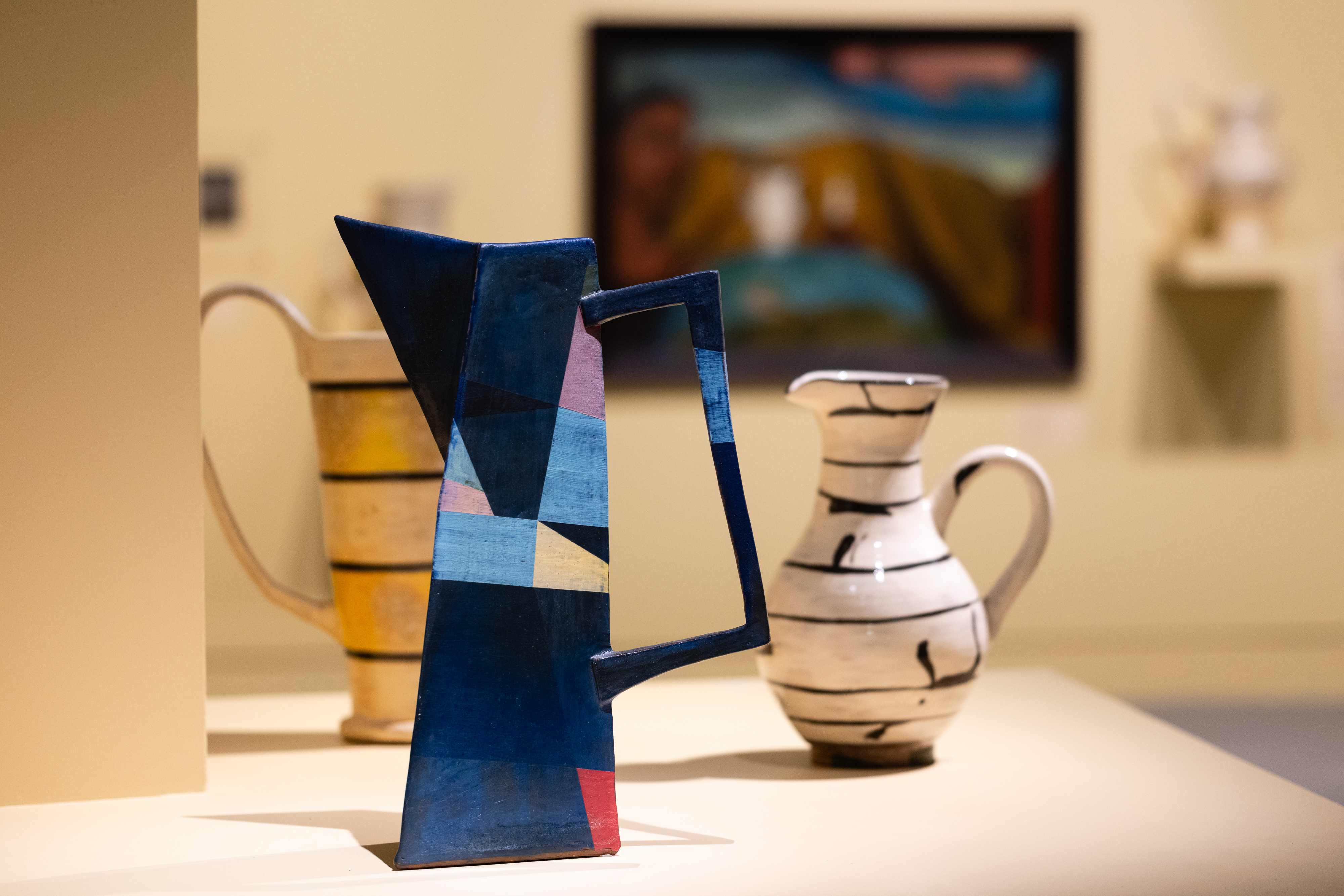 An installation shot of Paul Maseyk's jugs with the paintings they are responding to. This image features a three jugs in the foreground made by Paul Maseyk, with a large Colin McCahon painting in the background.