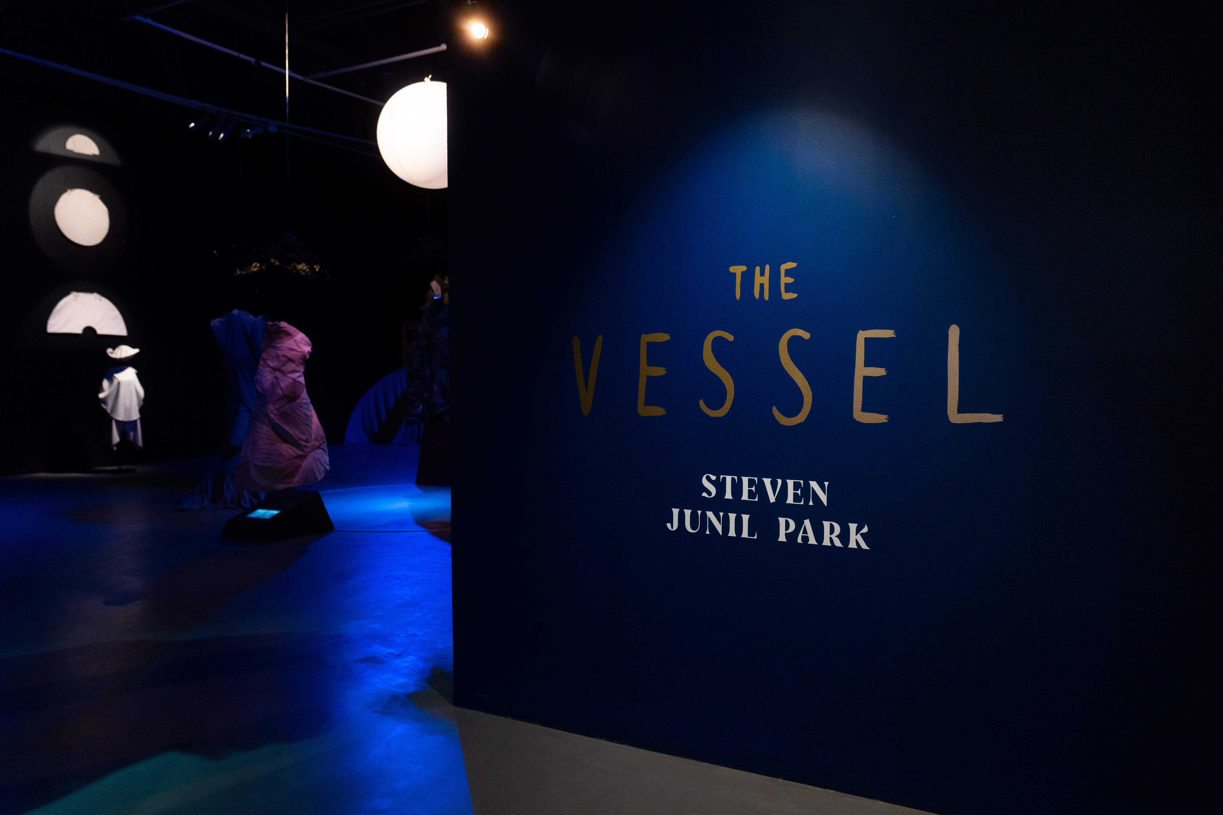 Title wall with words 'The Vessel' and sneak peek of costumes in background