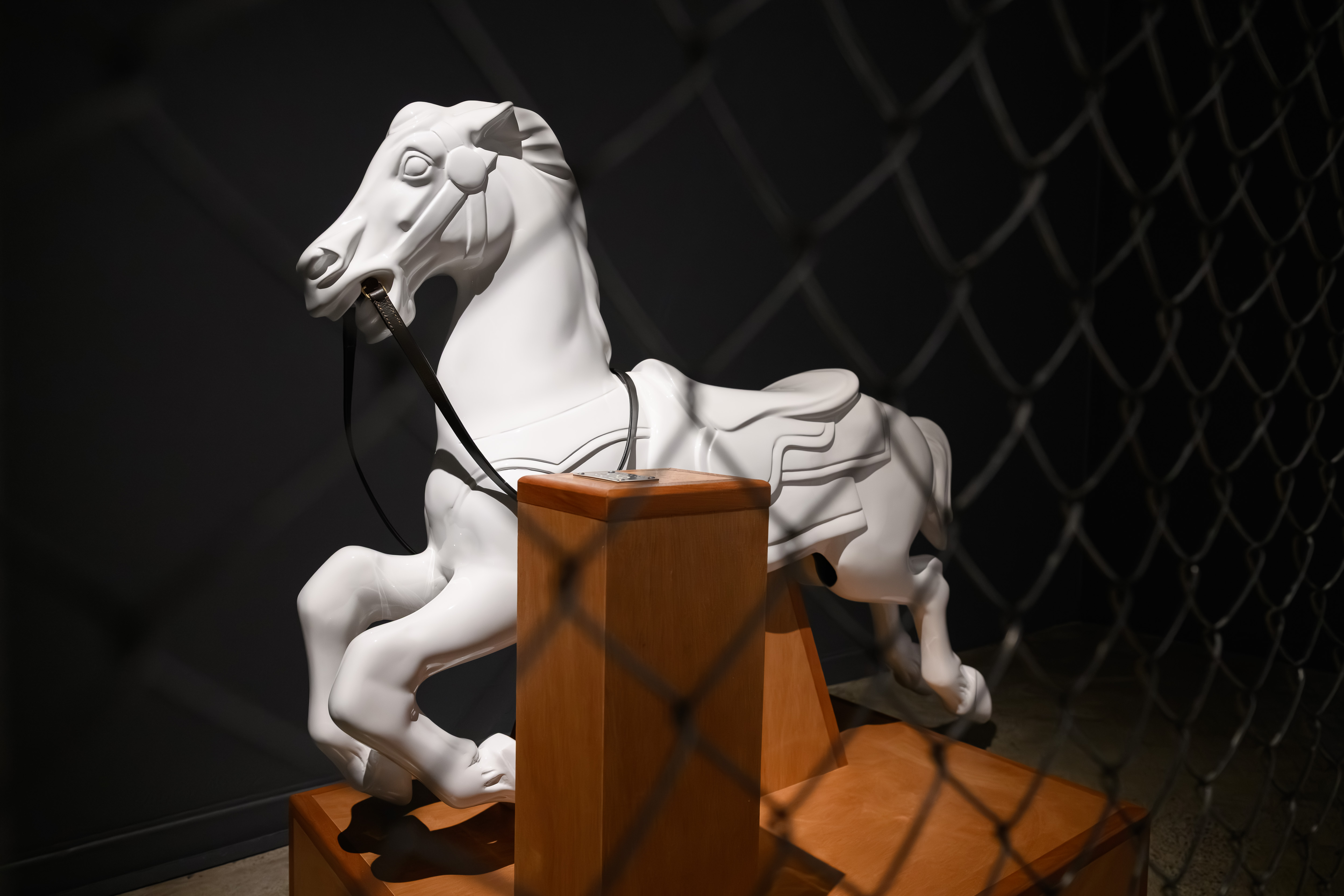 Sculpture of a white mechanical horse behind chain-link fence