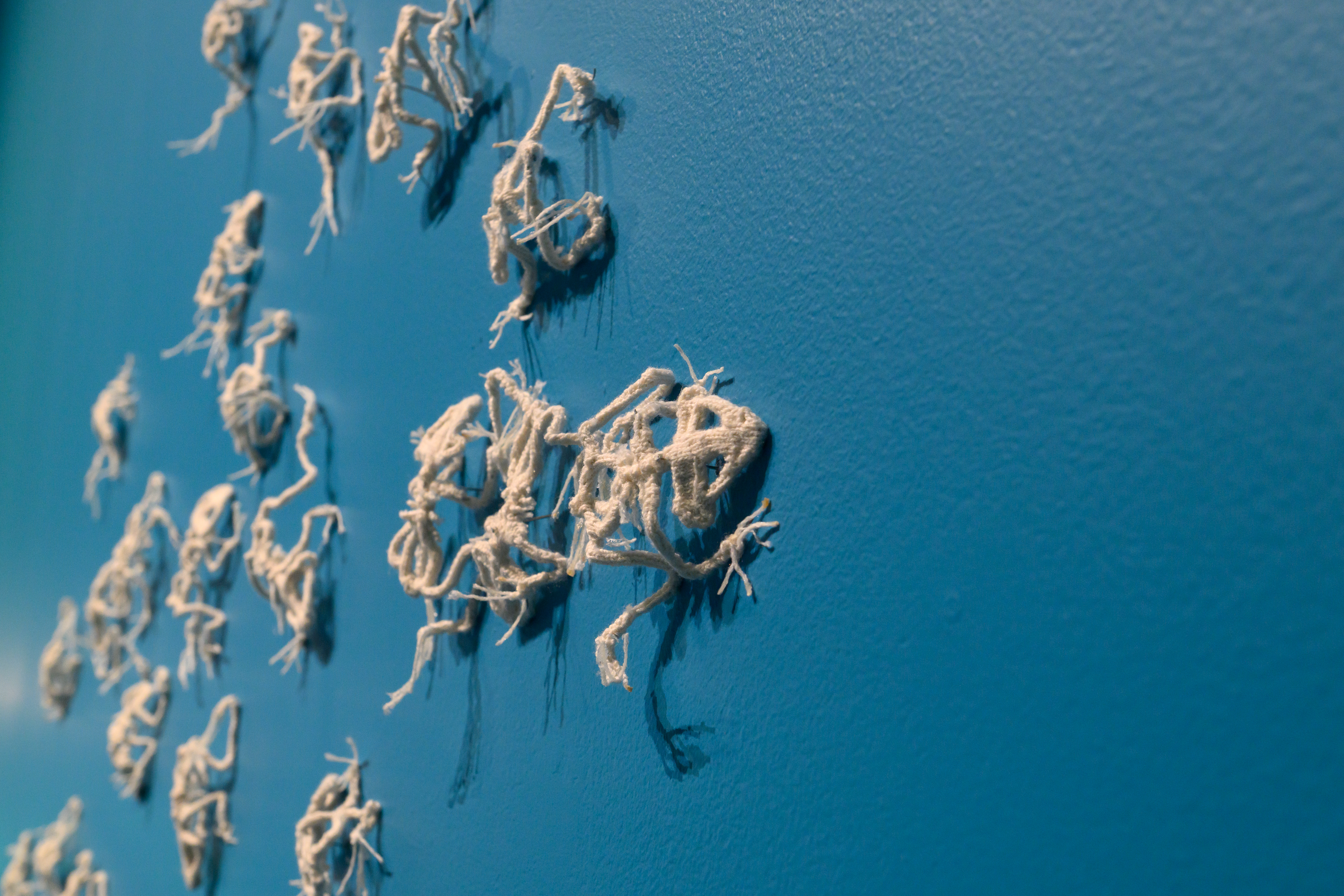 Close up of life-sized knitted frog skeletons, on a deep ocean blue background. 
